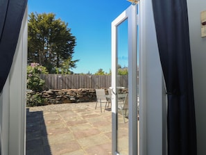Une porte-fenĂȘtre coulissante sâouvre sur un patio agrĂ©mentĂ© dâun mur en pierre, dâune clĂŽture en bois et dâune table avec des chaises.