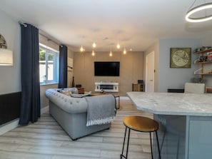 Un salon moderne avec un canapĂ© gris, un mur dâaccent en bois, un tĂ©lĂ©viseur Ă Ă©cran plat et un coin cuisine dotĂ© dâun comptoir en marbre.