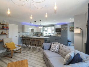 A modern kitchen with bar stools, a sofa with patterned cushions, and pendant lighting. - Ty Glan Morfa (Porthmadog)