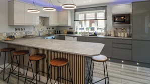 A modern kitchen with a large island, bar stools, and a microwave. - Ty Glan Morfa (Porthmadog)