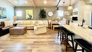 A spacious living room with a large sofa, a coffee table, and a dining area with a long table and bar stools. - `Accessible and Pet-Friendly: 2 Community Pools and a 1-Level Flat Entrance for Ultimate Comfort` (Port Aransas)