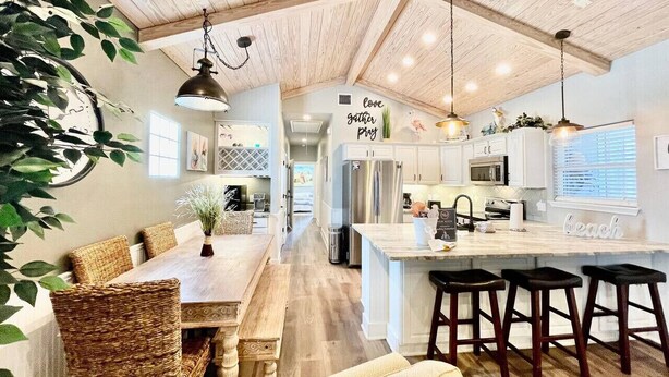 A modern kitchen with wooden ceiling beams, a dining area with wicker chairs, and a bar with stools. - `Accessible and Pet-Friendly: 2 Community Pools and a 1-Level Flat Entrance for Ultimate Comfort` (Port Aransas)