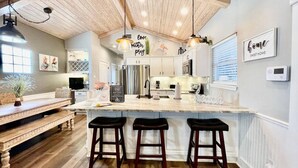 A kitchen with a wooden ceiling, white cabinets, a marble island with bar stools, and decorative wall art. - `Accessible and Pet-Friendly: 2 Community Pools and a 1-Level Flat Entrance for Ultimate Comfort` (Port Aransas)