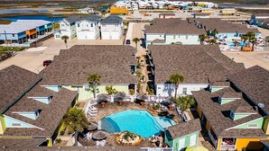 A residential area with colorful houses, a central swimming pool, and a view of the beach. - `Accessible and Pet-Friendly: 2 Community Pools and a 1-Level Flat Entrance for Ultimate Comfort` (Port Aransas)