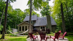 Ein Haus mit einer Terrasse, umgeben von Bäumen. Vier Adirondack-Stühle stehen auf der Terrasse.