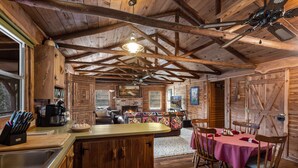 A rustic cabin interior with a wooden ceiling, a kitchen area with a bar, a dining table set for four, and a fireplace. - 22 miles to Round Top, 3/2 w/ trailer parking, relaxing cozy cabin w/ lake, wifi (La Grange)