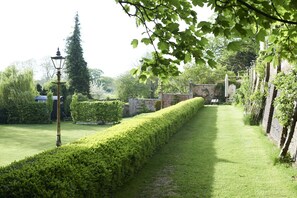 Un jardin bien entretenu, avec une haie soigneusement taillée, un lampadaire et un mur en briques.