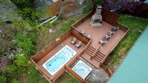 Un bain à remous et une cheminée sur une terrasse en bois, avec des sièges d’extérieur.