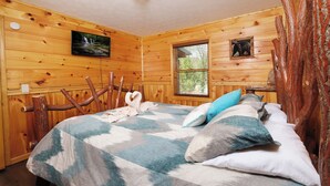 Une pièce de style cabane en bois, avec un lit, une chaise, une cheminée et un téléviseur fixé au mur.