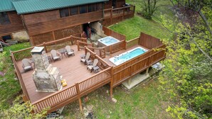 Une terrasse en bois avec des sièges d’extérieur, un jacuzzi et une vue sur un chalet.
