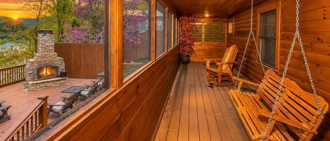 A wooden deck with a stone fireplace, outdoor seating, and a view of the landscape.