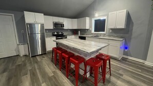 Una cocina moderna con armarios blancos, un refrigerador de acero inoxidable, un microondas, una estufa y una isla grande con taburetes rojos.