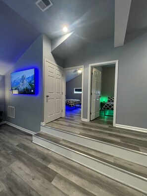 A modern hallway with a flat-screen TV mounted on the wall, wooden flooring, and a staircase leading to a bedroom with a bed and green ambient lighting. - Chic & Modern Stay walking distance to restaurants, bars and shops! (Louisville)