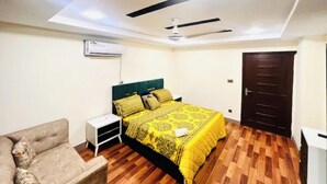 A bedroom with a bed, a nightstand, a chair, a ceiling fan, and a door. - Comfy apartment in Bahria town civic center. (Rawalpindi)