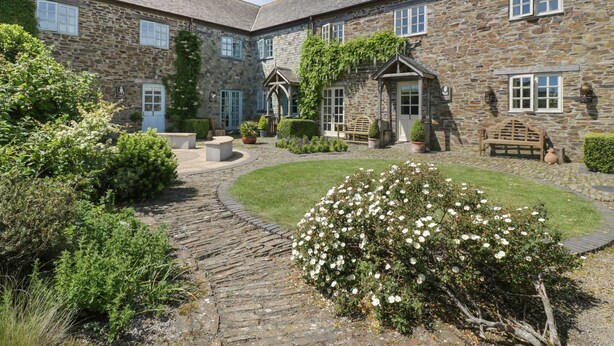 A stone building with a courtyard, stone benches, and a flower bush. - Dovecote (St Austell)