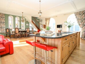 A spacious kitchen with a central island, wooden cabinets, and a red bar stool. - Ty Biwmares (Beaumaris)
