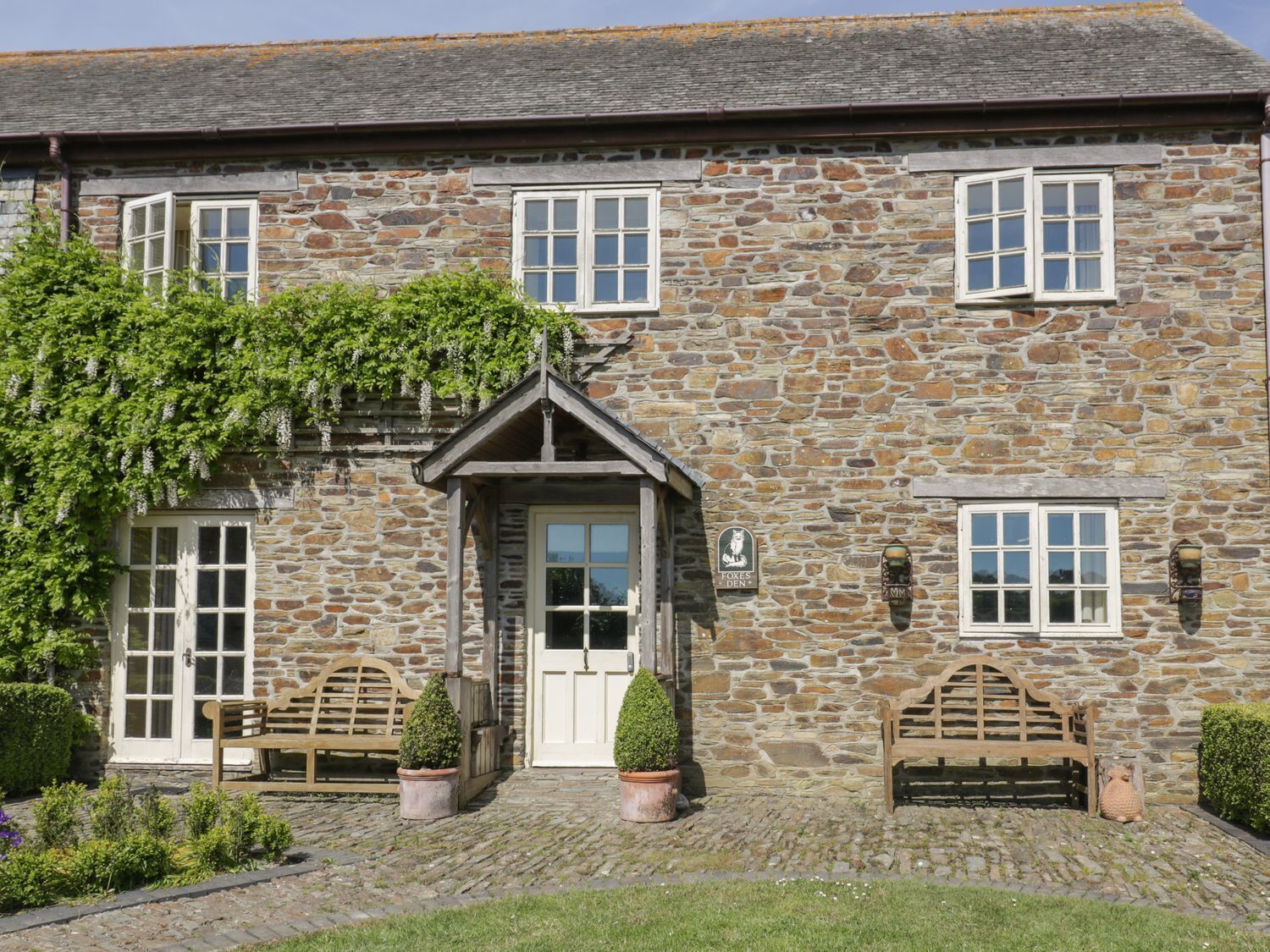 A stone building with a traditional design, featuring a central entrance with a door and windows, and two benches outside.