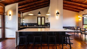 A spacious kitchen with a large island, wooden ceiling beams, and modern pendant lighting. - Stunning Clifftop Villa with Infinity Pool (Westerhall Land Settlement)