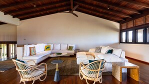 A spacious living area with a high ceiling, a white sofa set, two wicker chairs, a small round table, and a ceiling fan. - Stunning Clifftop Villa with Infinity Pool (Westerhall Land Settlement)
