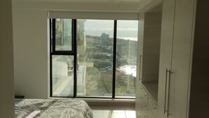 A bedroom with a large window, a bed with a patterned bedspread, and a wardrobe. - Ocean Front Suite Apartment in Manta Poseidon Building (Manta)
