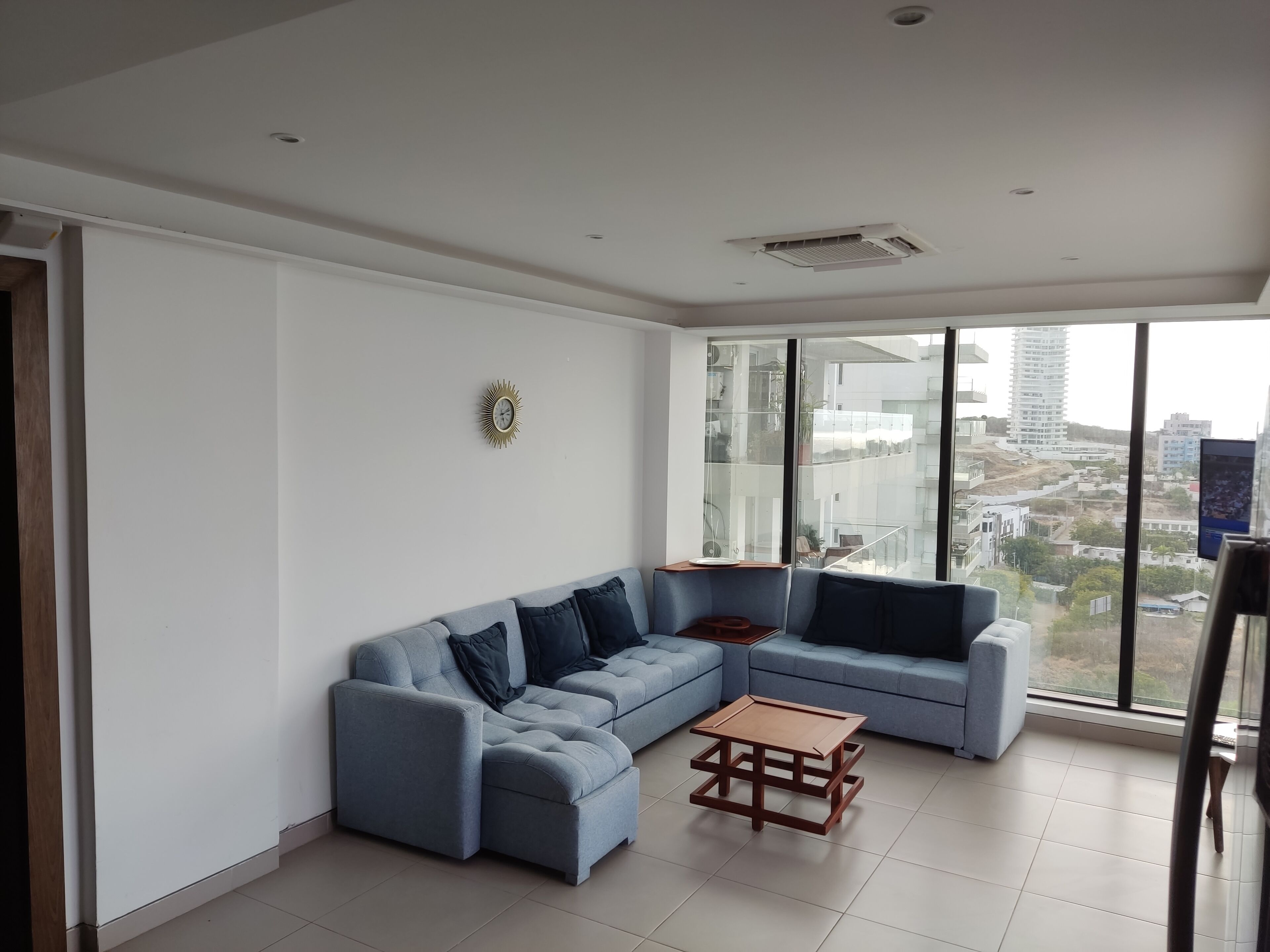 Una sala de estar moderna con un sofá modular, una mesa de centro de madera y un ventanal con vistas a la ciudad.