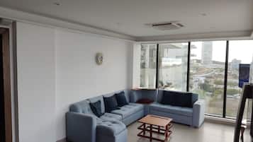 Una sala de estar moderna con un sofá modular, una mesa de centro de madera y un ventanal con vistas a la ciudad.