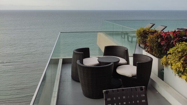 A balcony with wicker furniture, a view of the sea, and a glass railing. - Ocean Front Suite Apartment in Manta Poseidon Building (Manta)
