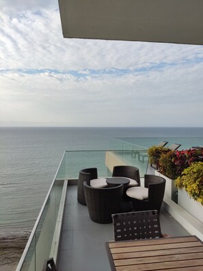 A balcony with wicker furniture, a view of the sea, and a glass railing.