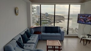 A modern living room with a large window offering a city and coastline view. - Ocean Front Suite Apartment in Manta Poseidon Building (Manta)