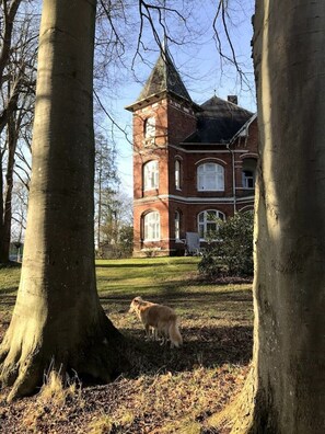 Un grand bâtiment en briques, doté d’une tour, entouré d’arbres et d’une zone herbeuse.