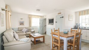 Ein gemütliches Wohnzimmer mit einer Couch und einem Couchtisch, ein Holzesstisch mit Stühlen sowie eine Küchenzeile mit Fenster und Tür.