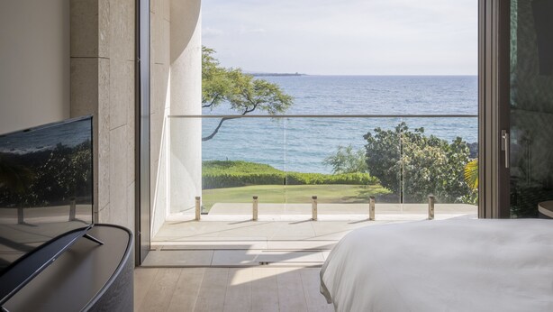 A bedroom with a large sliding glass door leading to a balcony overlooking a beach and ocean.