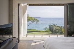 Un dormitorio con un amplio ventanal corredero que da a un balcón con vistas a la playa y al océano.