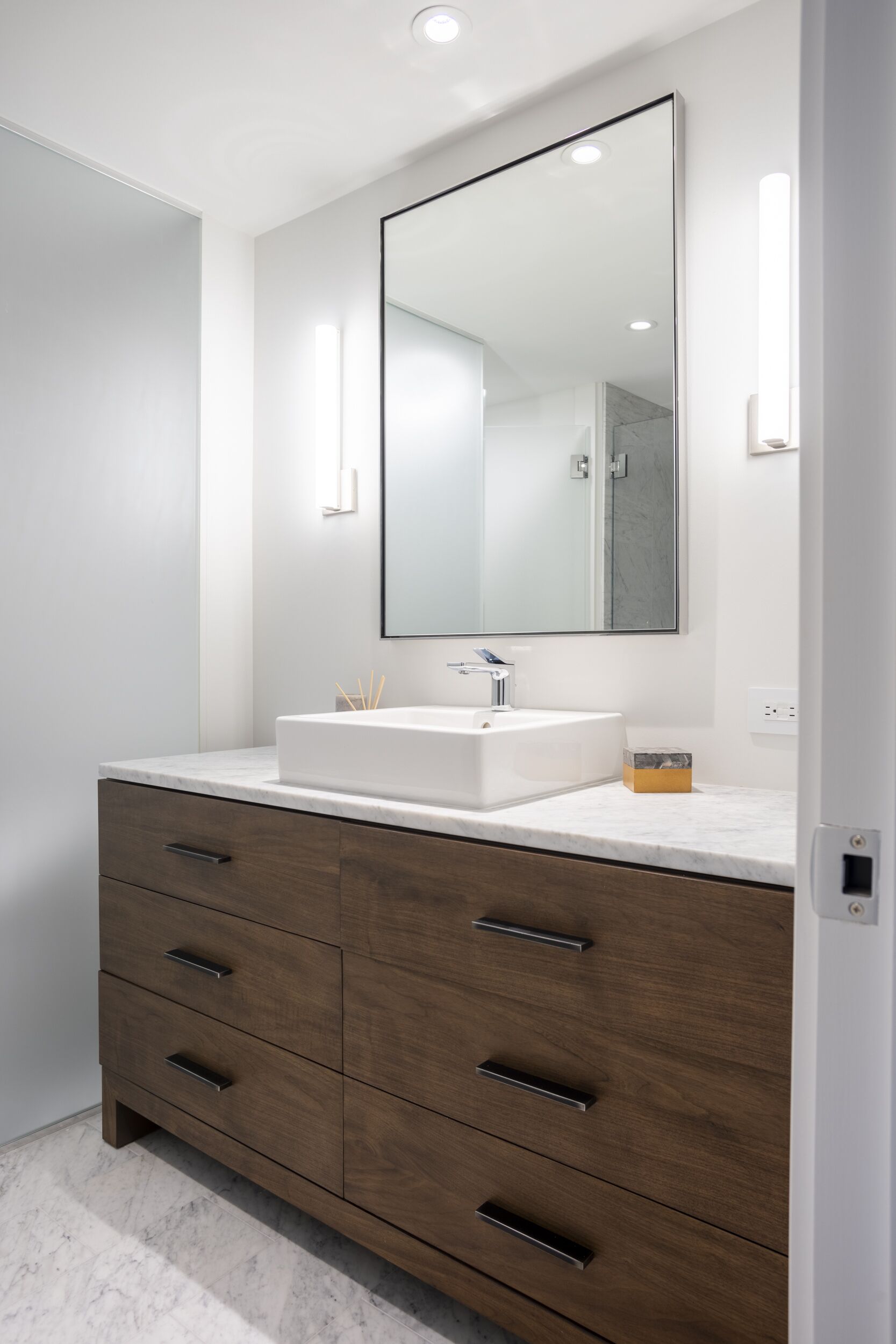 A modern bathroom with a white sink, a large mirror, and wooden cabinetry.