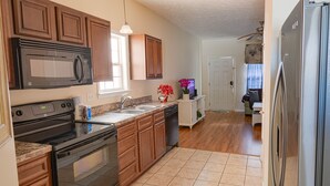 A kitchen with wooden cabinets, a black stove, a microwave, and a refrigerator. - 2-Bedroom Cottage, One Block to Beach! Free WIFI, Free Parking (Myrtle Beach)
