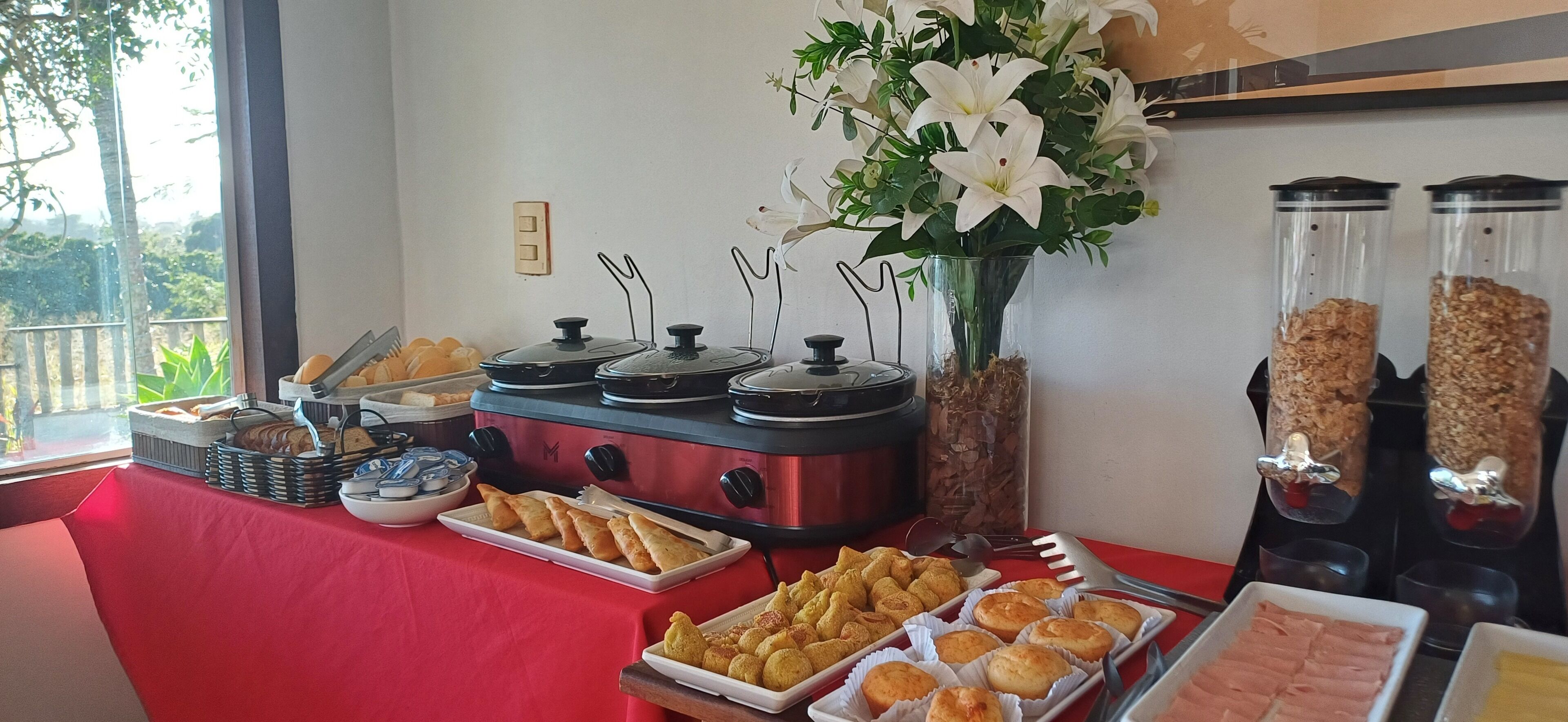 A buffet table with various food items, a vase of flowers, and a view of the outdoors.