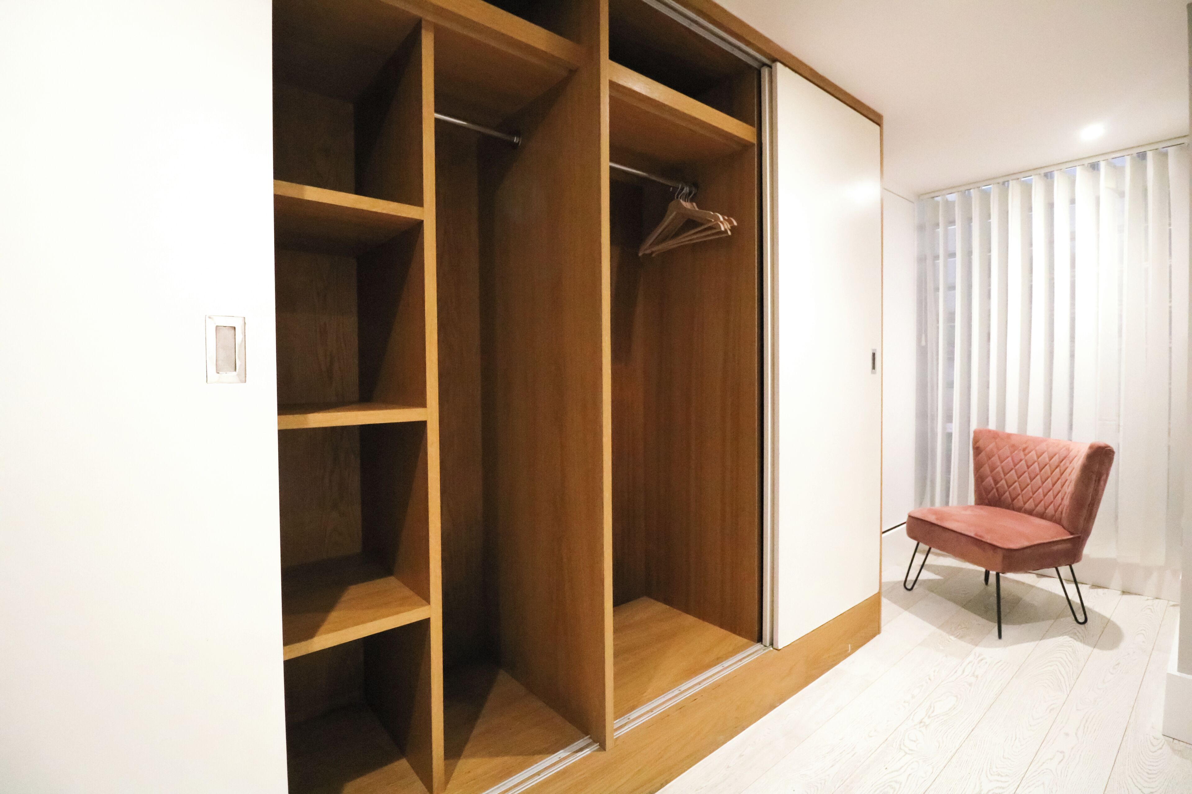 A walk-in closet with multiple shelves and a hanging rod, a red chair, and a window with blinds.