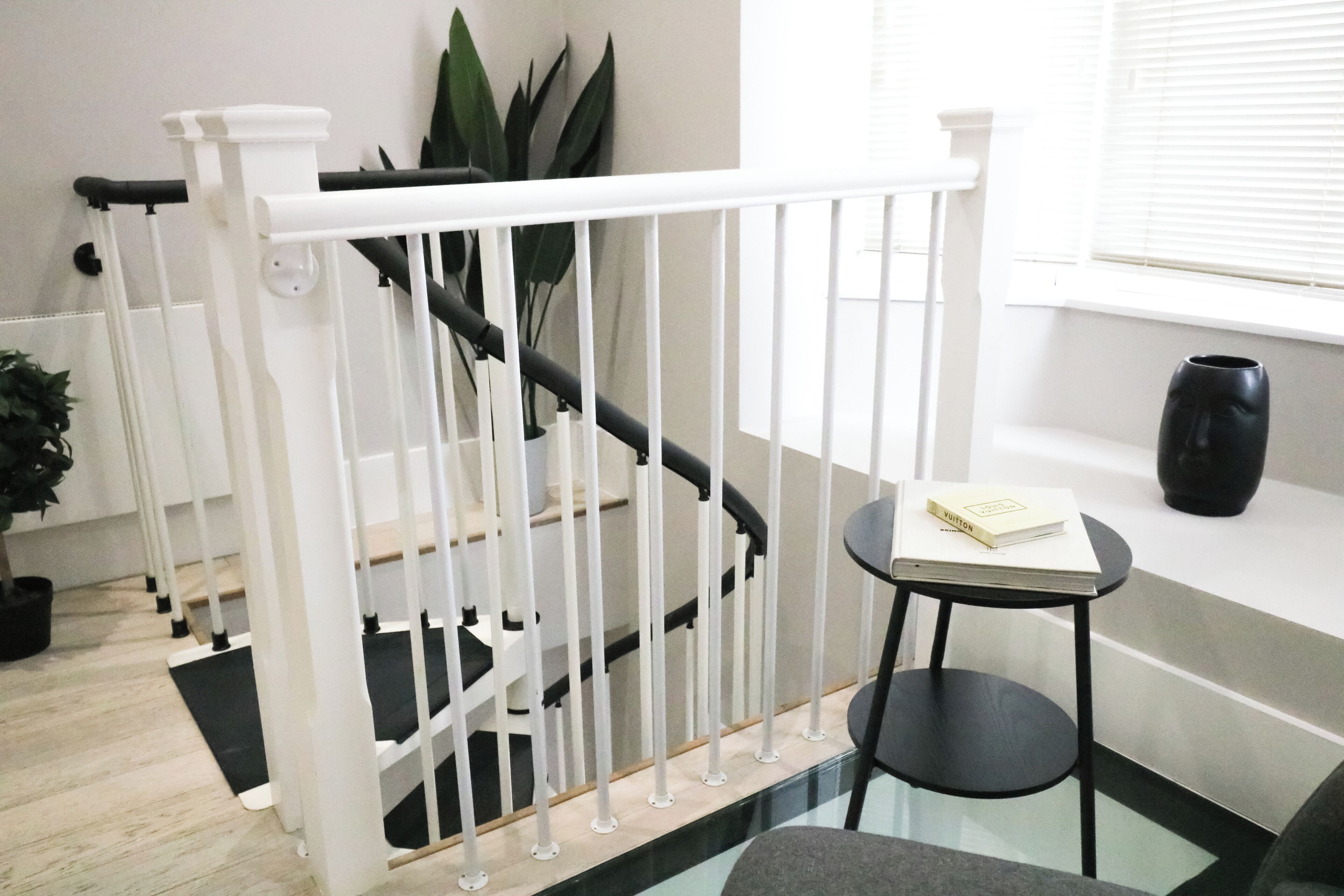 Un escalier moderne avec des rampes blanches, une petite table ronde sur laquelle repose un livre, et une plante en pot.