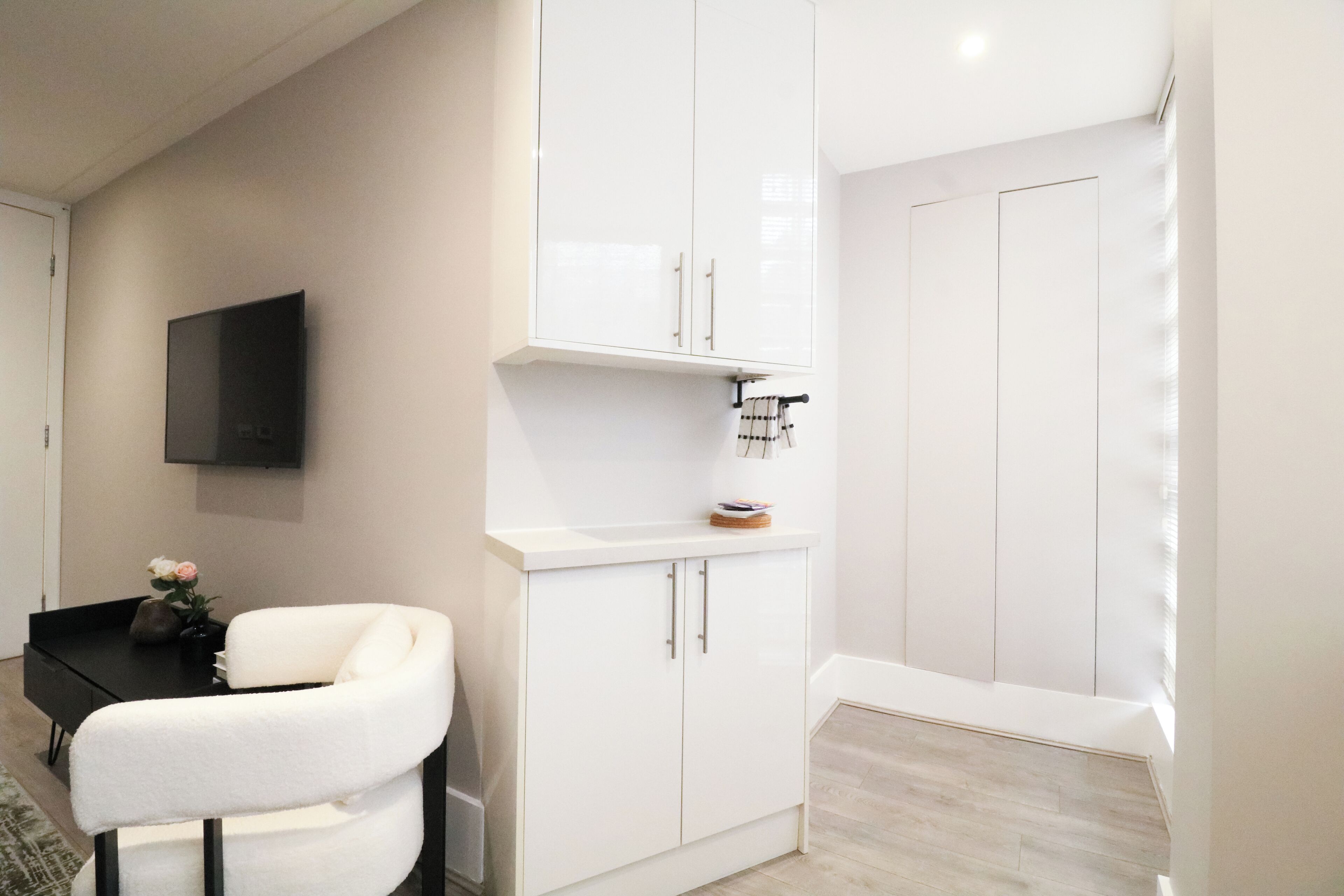Une chambre moderne avec un canapé blanc, un téléviseur à écran plat fixé au mur et une armoire blanche dotée d’un miroir.