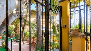 A courtyard with a yellow wall, a metal gate, and potted plants.