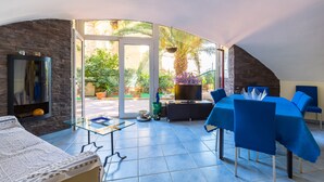 A sunlit patio with a dining table and chairs, a sofa, and a television.