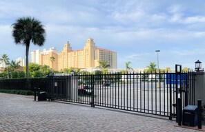 A gated parking area with a paved walkway, palm trees, and a large building with multiple towers in the background.