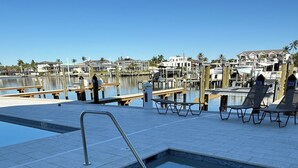 A swimming pool with a metal ladder, surrounded by a tiled deck and wooden benches. - Remodeled Condo, Steps to the Beach (Naples)