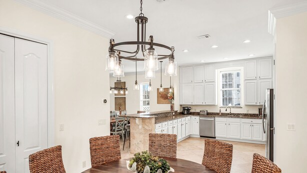 A modern kitchen with white cabinets, a central island, and a dining area with wicker chairs and a wooden table. - 9 Bedrooms / 6.5 Baths / Sleeps 28 / 8 Parking Spots / Pool / Steps to Beach!!! (Destin)