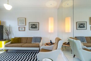 A modern living room with a sofa, armchairs, and a coffee table. There are framed pictures on the wall and a large mirror reflecting the room. - Top Floor Darlinghurst/Sydney Views Walk To CBD (Darlinghurst)