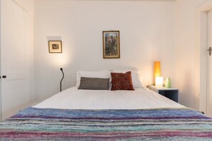 A bed with a colorful blanket, two pillows, a bedside lamp, and a framed picture on the wall.