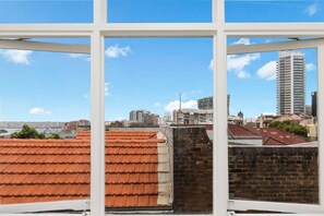 A view through a window of a cityscape with red-tiled roofs and a variety of buildings. - Top Floor Darlinghurst/Sydney Views Walk To CBD (Darlinghurst)