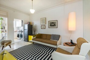 A modern living room with a sofa, a coffee table, and a striped rug. There is a kitchen area with appliances visible. - Top Floor Darlinghurst/Sydney Views Walk To CBD (Darlinghurst)