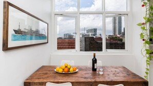 A dining area with a wooden table, a plate of oranges, a bottle of wine, and a framed picture of a ship on the wall. - Top Floor Darlinghurst/Sydney Views Walk To CBD (Darlinghurst)