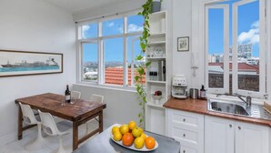 A modern kitchen with white cabinets, a wooden table, and a large window with a city view. - Top Floor Darlinghurst/Sydney Views Walk To CBD (Darlinghurst)